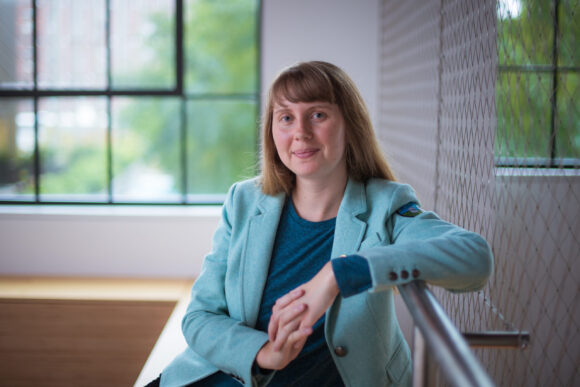 Skylar Larsen sits indoors, arm on railing, with windows and a wire wall in background.