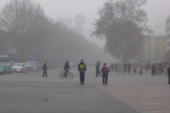 Photo of pedestrians at a tree-lined intersection, all seen through a polluted haze in Anyang City, China