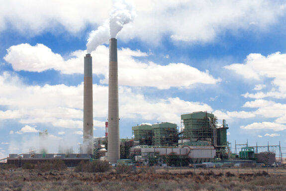 Photo of a power plant with two smokestacks in a desert area on a partly cloudy day.