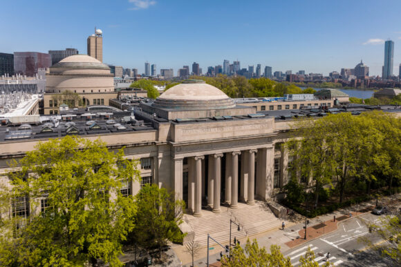 Aerial view of MIT campus building entrance with Boston skyline in the distance.