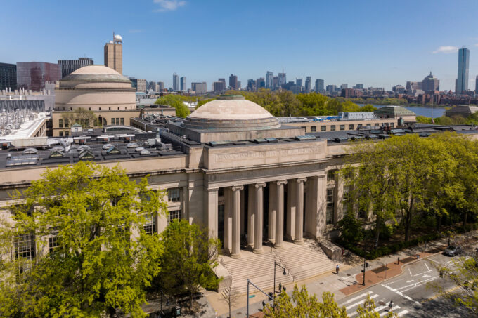 Aerial view of MIT campus building entrance with Boston skyline in the distance.
