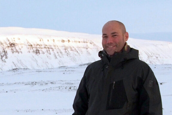 Brent Minchew smiles at the camera in front of an expanse of snow and ice.