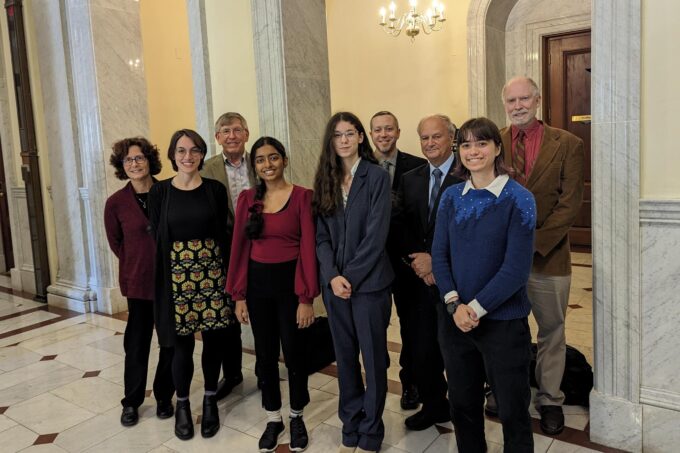 Erin Cusson, Prajna Nair, Ella Sheffield, and Tim Brothers stand in a group of nine people inside the Massachusetts Statehouse.