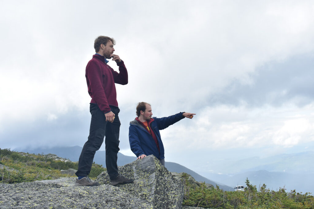 Milan Kloewer and Robert van der Drift stand on top of a rock, looking off and pointing at something out of frame.
