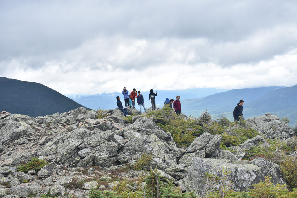 Ten people stand on top of a rocky outcropping some distance from the camera.