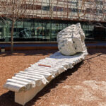 Sculpture by Julian Charriére: a large glacial erratic boulder drilled with holes, installed in front of Building 55 sitting on top of its own drilled core samples.