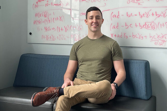 Justin Cole sits on a couch in front of a whiteboard of math equations.
