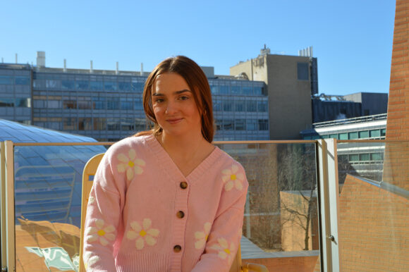 Katie Kempff sits outside on a balcony in nice weather, smiling at the camera.