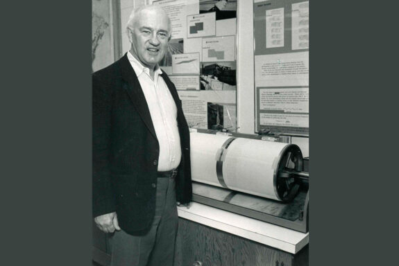 A black and white photo of Lynn Sykes standing next to an old-fashioned rotating drum seismograph.