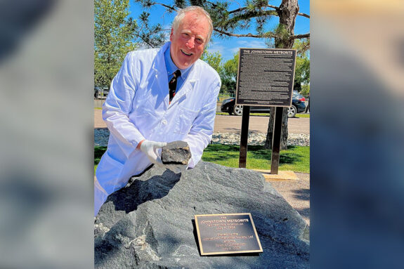 Professor Richard Binzel smiles while holding a meteorite fragment next to a plaque commemorating the day it fell in Johnstown, Colorado, in 1924.