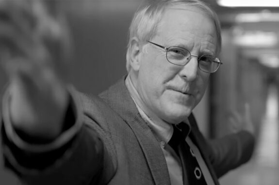 A black and white image of Richard Binzel with his hands stretched out along the Infinite Corridor.