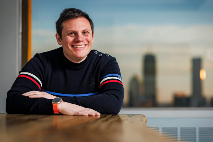 Andrew Babbin sits inside with Boston skyline in background.