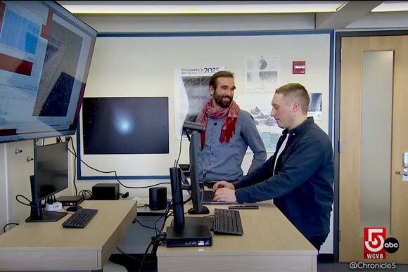 Julien de Wit is talking with Artem Burdanov while he types at a computer.