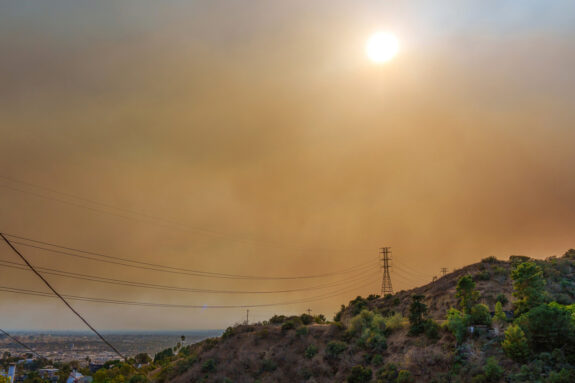 Photo of the sun peeking through orange smoggy air over a hillside, with Los Angeles in the background.