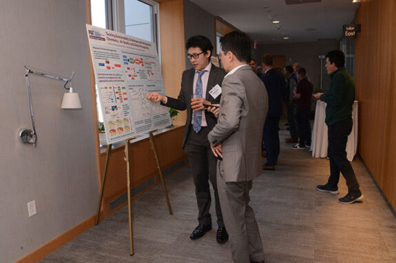Anthony Wong stands at a research poster while explaining it to another person.