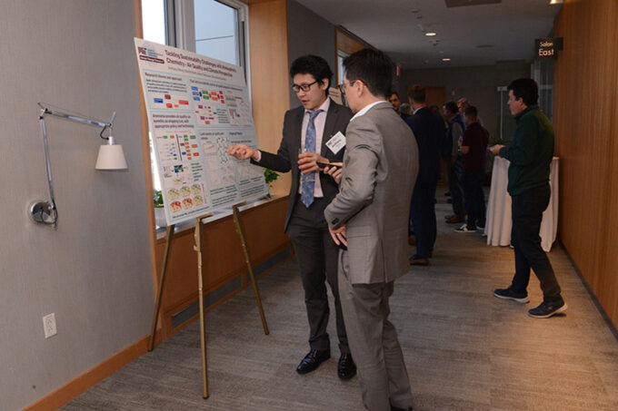Anthony Wong stands at a research poster while explaining it to another person.