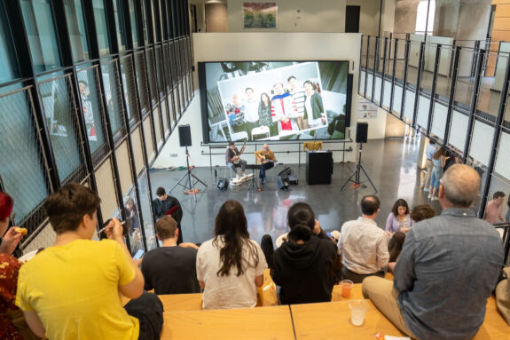Looking down at the crowd from the top of the bleachers in the Building 55 atrium during the EAPS commencement reception toward a guitarist and banjo player.