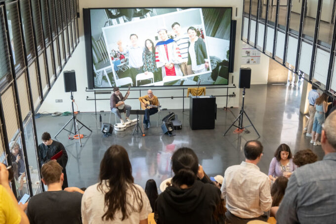 Looking down toward a guitarist and banjo player from the top of the bleachers filled with seated guests in the Building 55 atrium during the EAPS commencement reception.