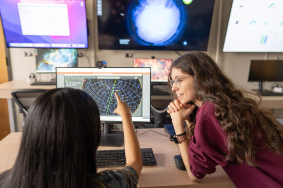 Two students confer in front of an array of monitors with astronomy data.