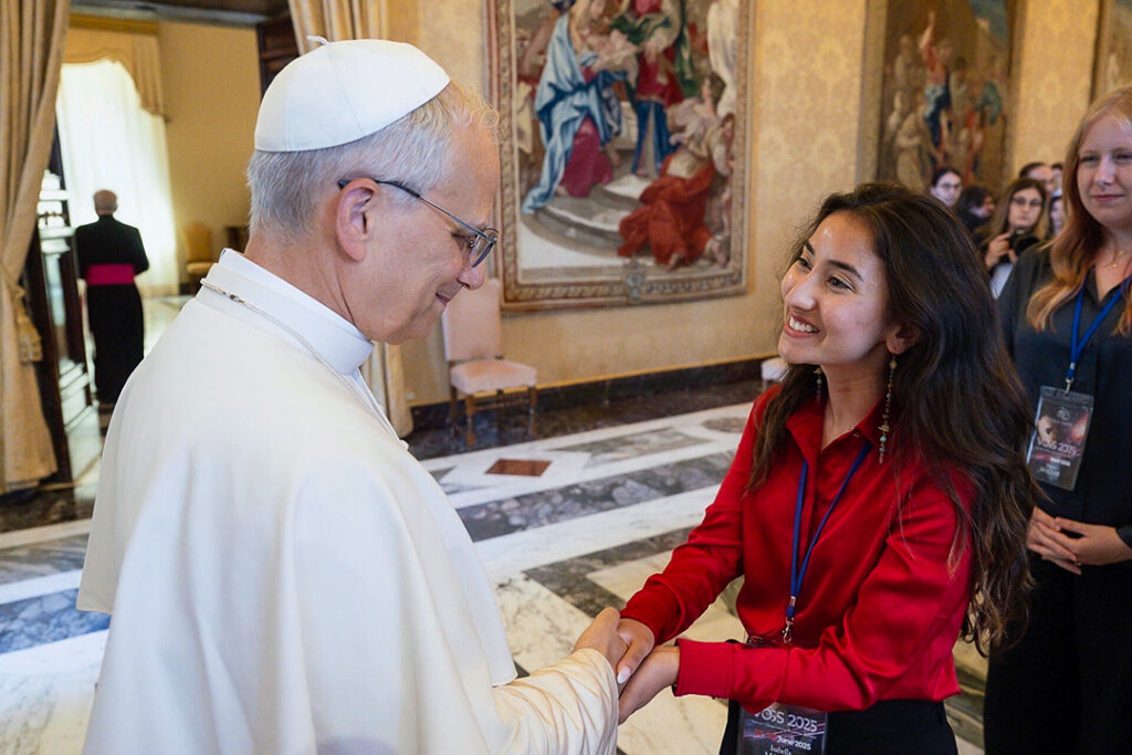 Isabella Marcias shakes hands with Pope Leo XIV. She is wearing a bright red shirt.