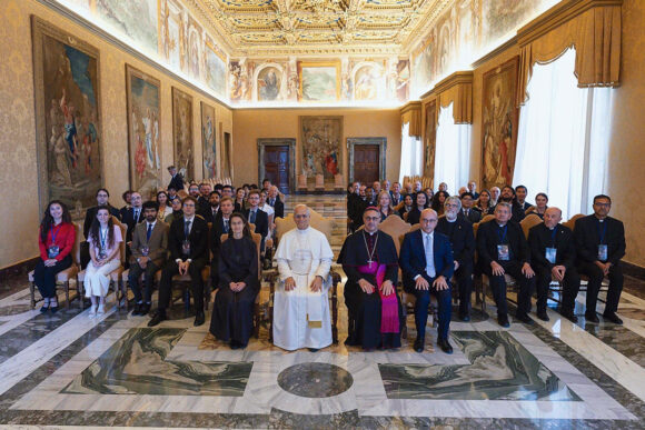 Pope Leo XIV sits in the center of a front row with three other Vatican officials; behind him are six rows of students and scientists involved with the Vatican Observatory Summer School program.