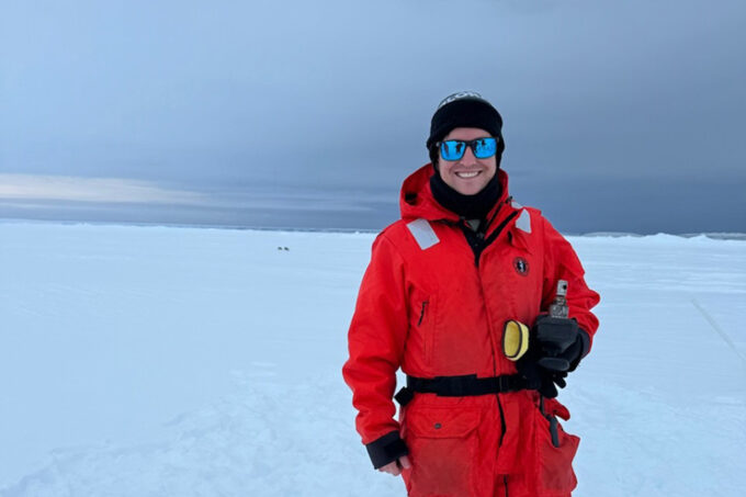 Ryan Woosley in an orange suit and on a large stretch of snow in Antarctica.