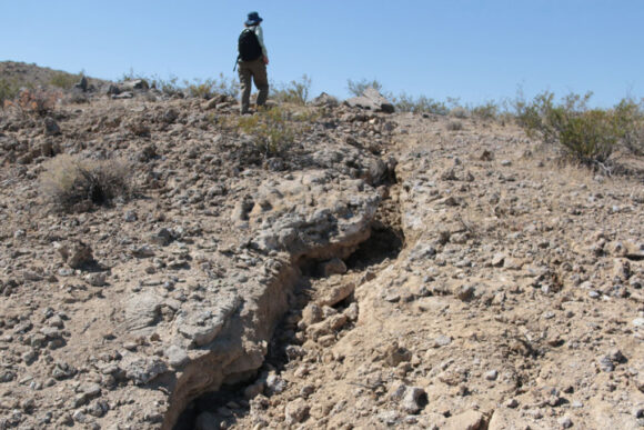 A figure can be seen standing near a marge crack in the ground caused by the 2019 Ridgecrest earthquake.