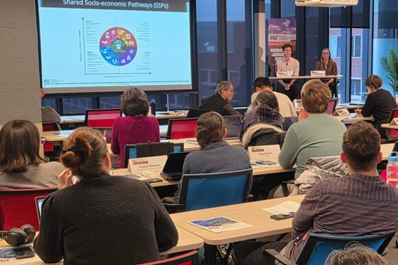 Two presenters at the front of a crowded room giving a lecture.