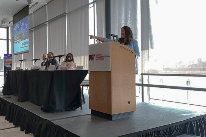 Jennifer Morris stands at a podium and is pointing to the audience during the 48th MIT Global Change Forum while moderating a panel.