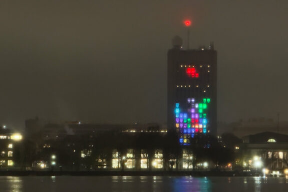MIT's famous Green Building from across the Charles River, its windows lit up to show a rainbow color Tetris board.