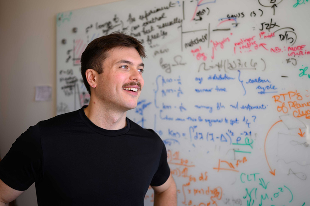Perrin Davidson in front of a whiteboard filled with scientific equations.