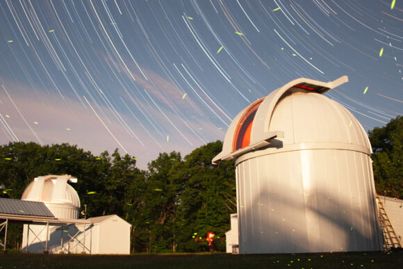A time-lapse photo of a telescope dome at the Wallace Astrophysical Observatory. Star tracks, as well as firefly tracks, can be seen in the sky.